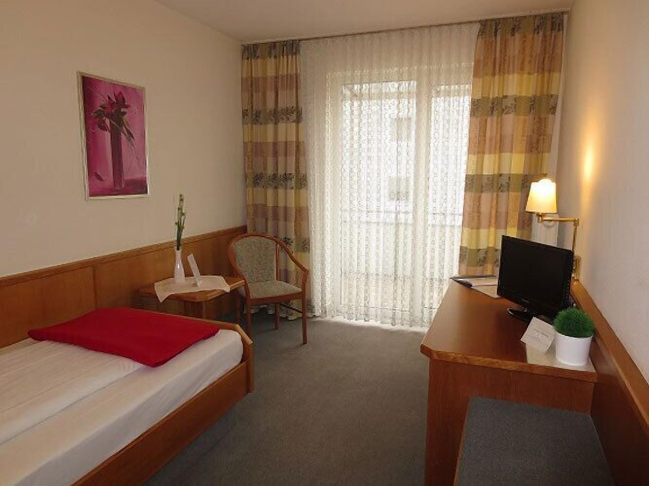 A hotel room with two single beds, a desk with a computer, a chair, and a small table with a vase.
