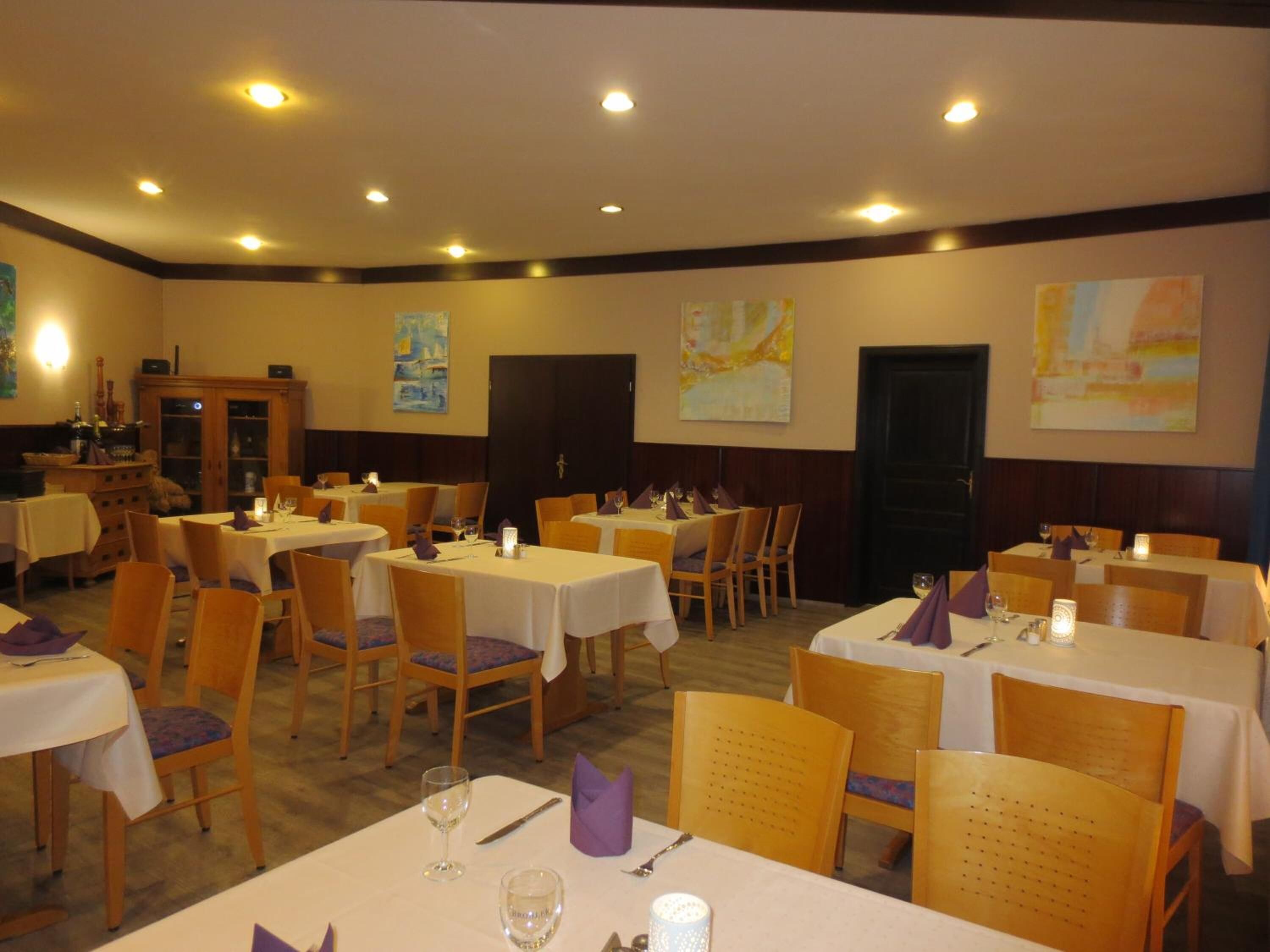 A dining area with multiple tables and chairs, each set with a white tablecloth and purple napkins.