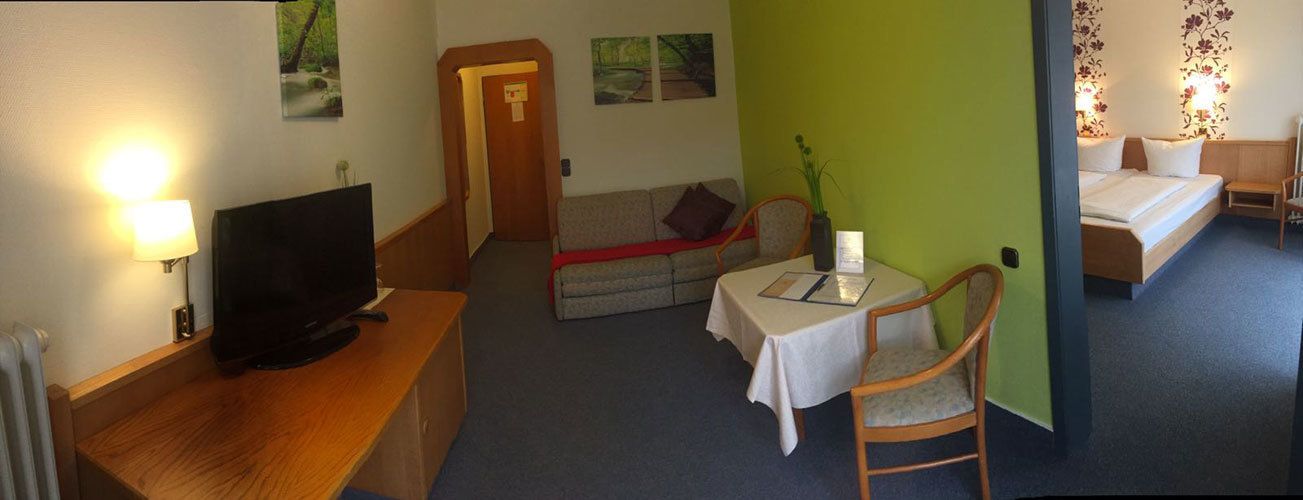 Una habitación de hotel con televisión, una mesita de noche con lámpara, sofá y cama.