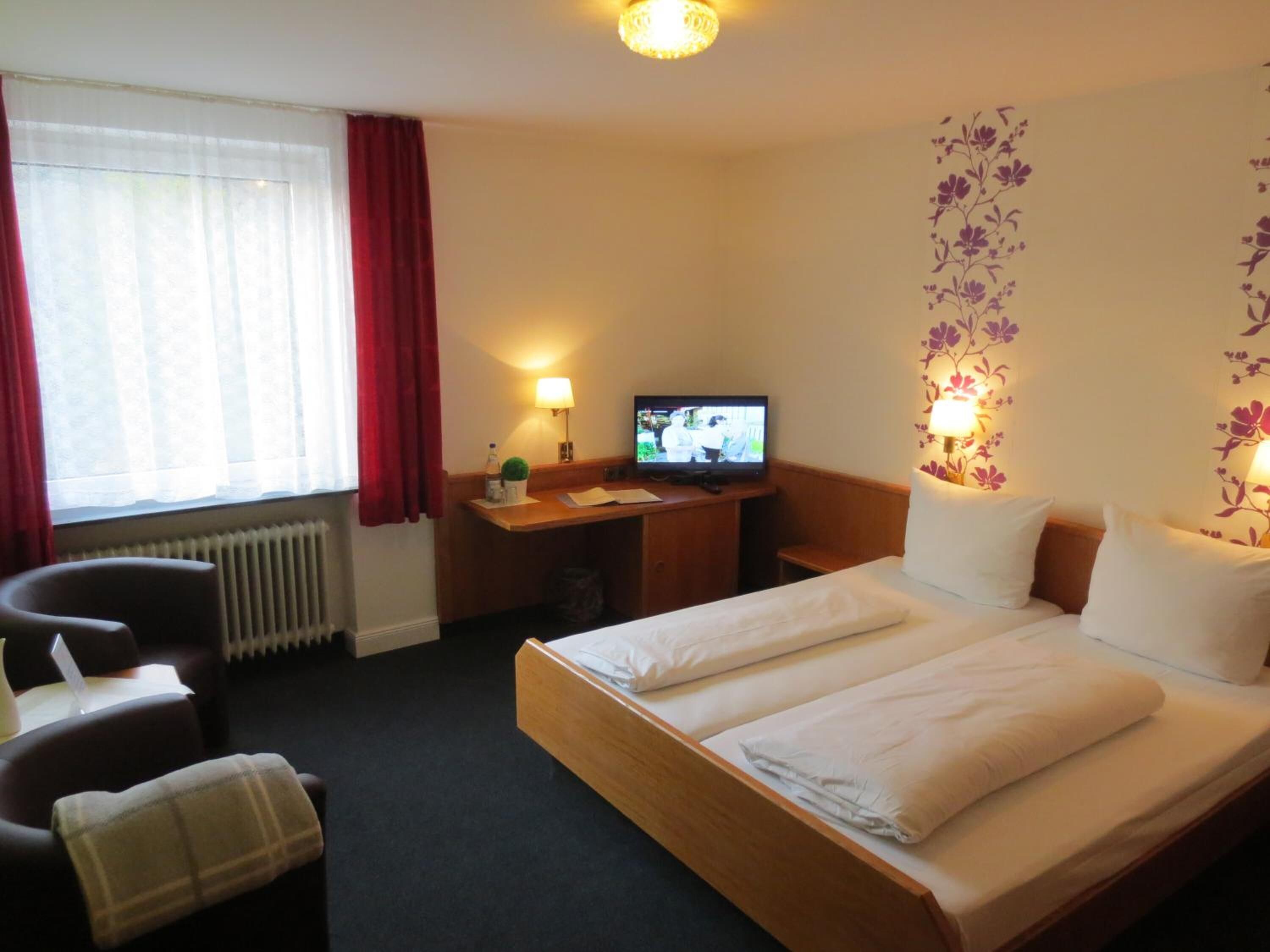A hotel room with a bed, a desk, a television, and a chair.