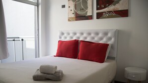 A neatly made bed with a white headboard and red pillows, a small bedside table, and artwork on the wall. - Chile & 9 de Julio (Buenos Aires)