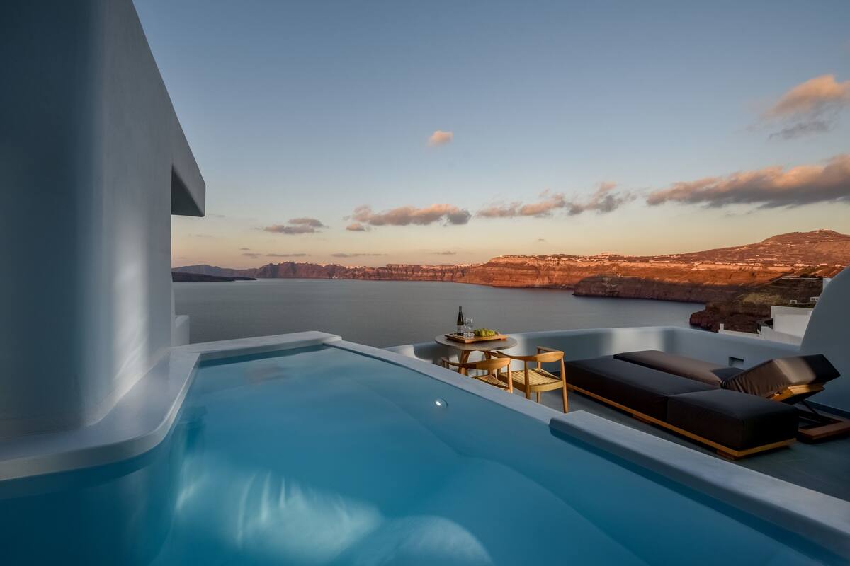 Una piscina infinita moderna con vistas a un paisaje costero, que incluye un cuerpo de agua y montañas distantes.