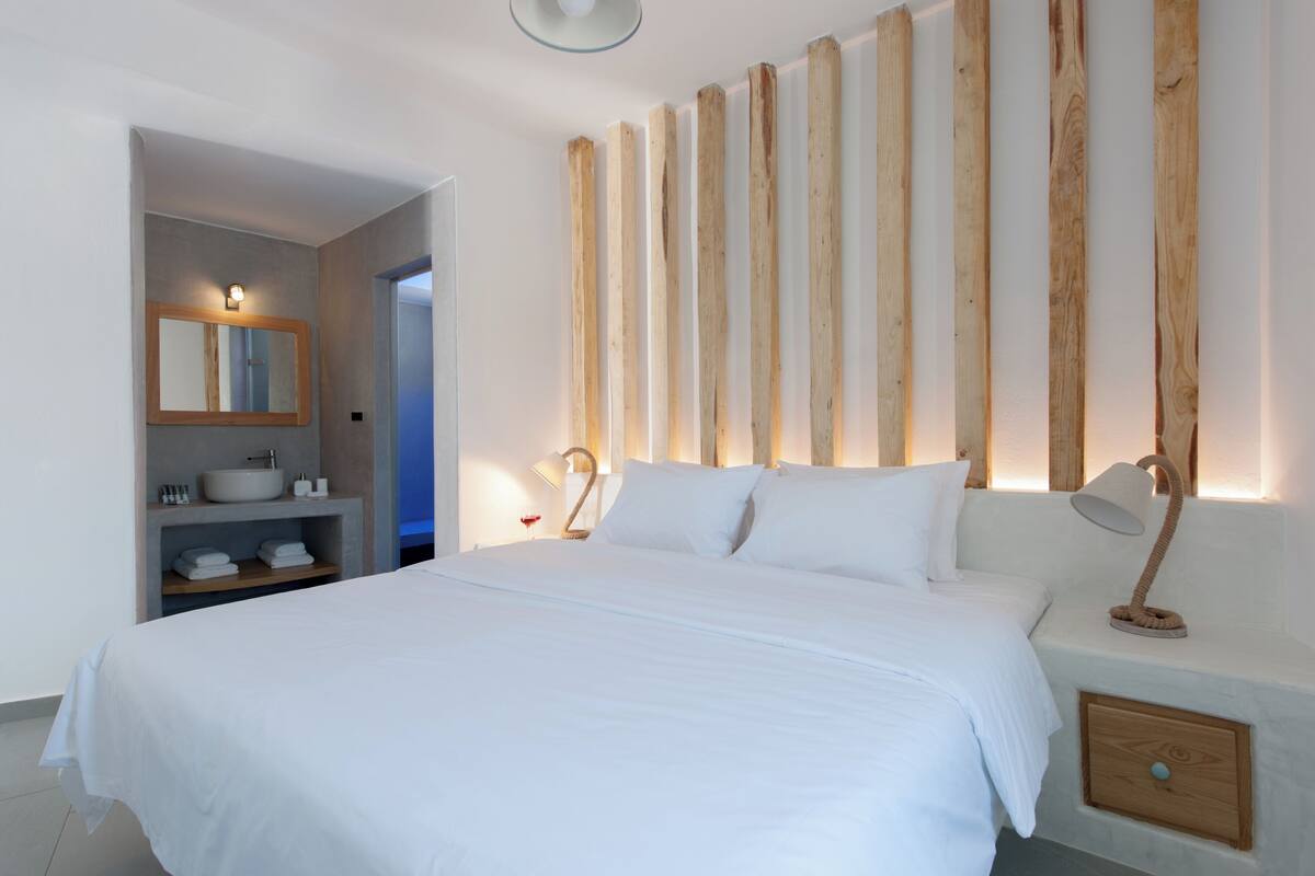 Un dormitorio con una cama grande, una mesita de noche con lámpara, un mueble auxiliar, un estante empotrado con espejo y un panel de pared de madera.