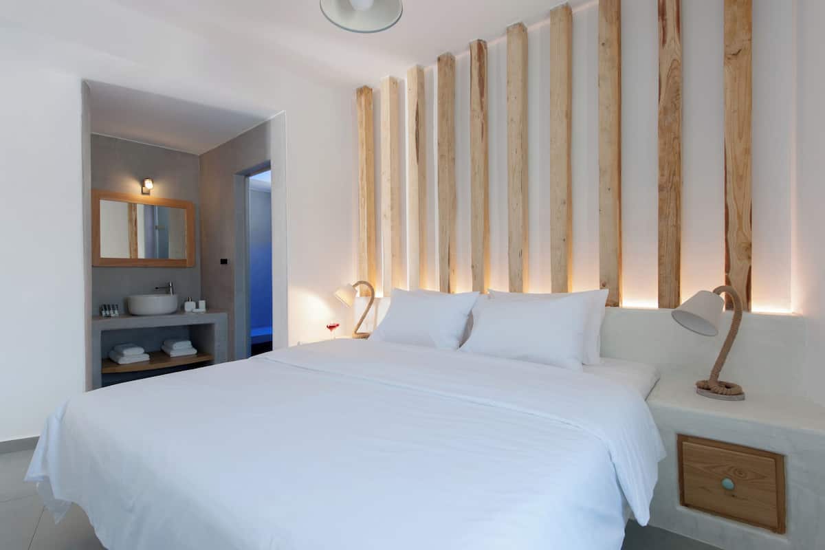 Une chambre avec un grand lit, une table de chevet avec une lampe, une commode, une étagère intégrée avec un miroir et un panneau mural en bois.