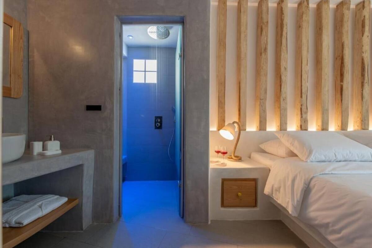 Un dormitorio moderno con cama, mesita de noche y tocador. Hay un baño con lavabo y espejo.