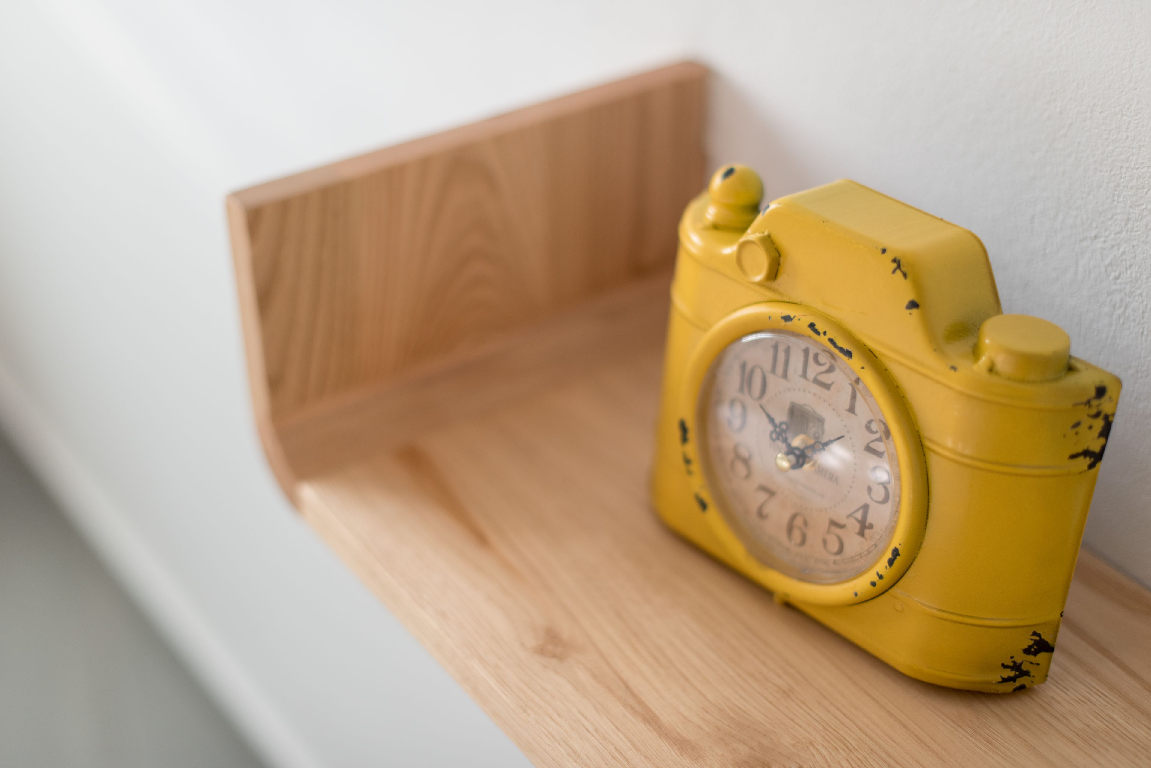 A yellow analog clock with a wooden shelf.