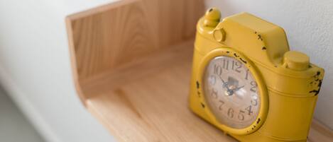 A yellow analog clock with a wooden shelf.