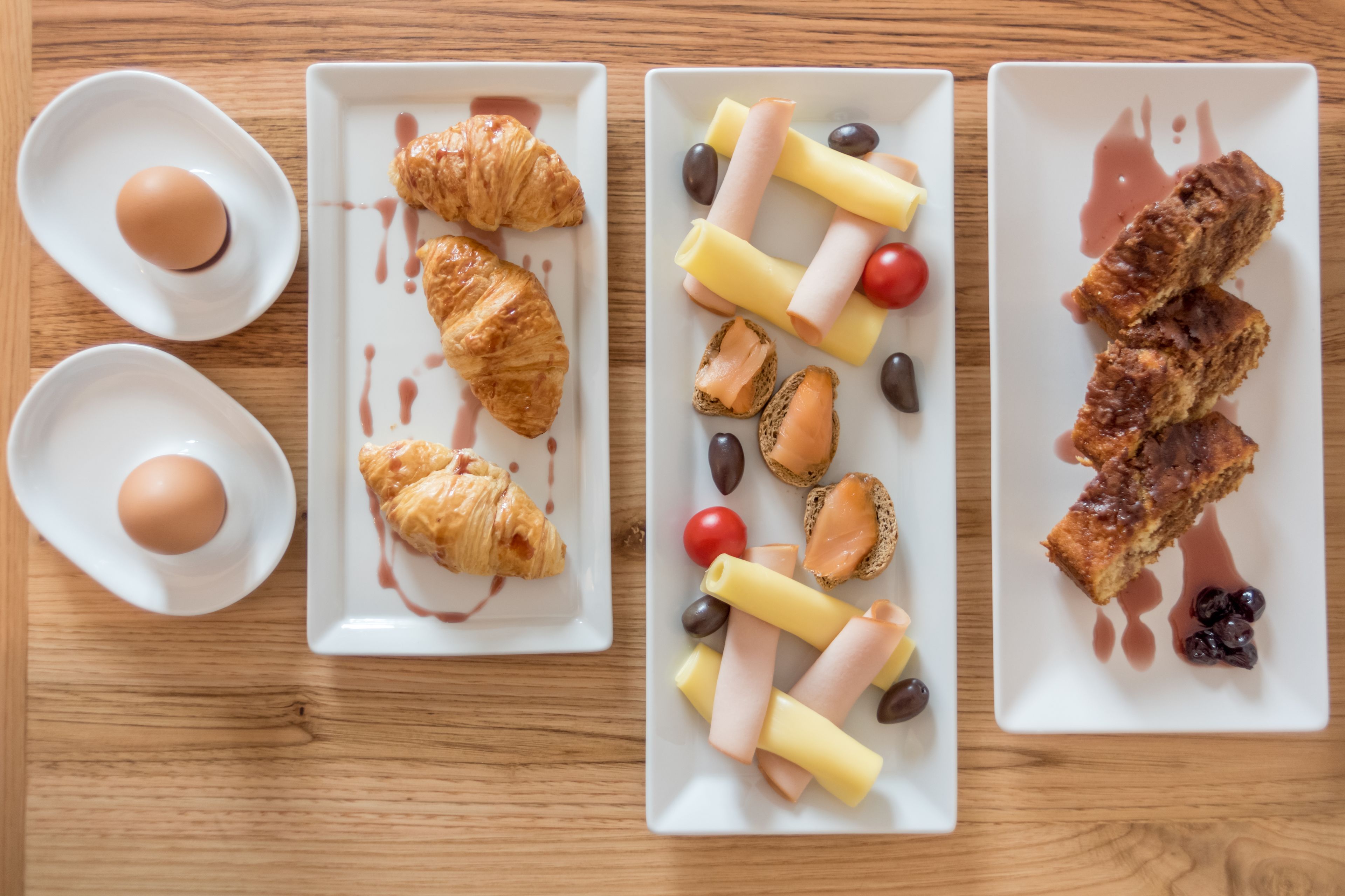 Three white rectangular plates with food items on a wooden table.