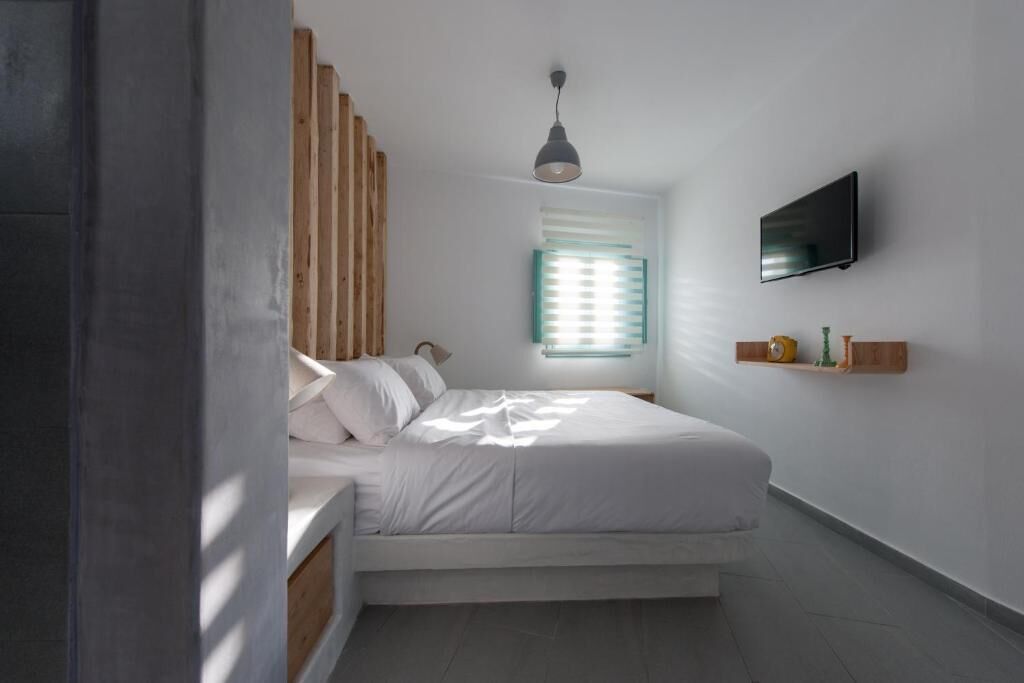 A bedroom with a bed, a TV mounted on the wall, and a window with blinds.