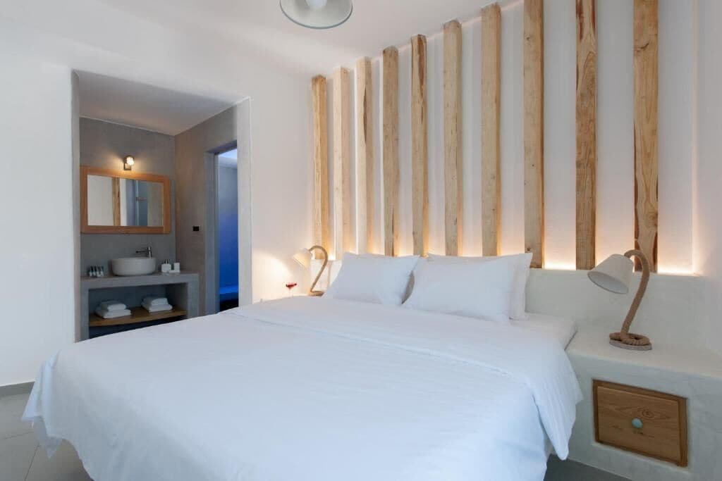 Una camera da letto con un letto grande, un pannello murale in legno, un comodino con una lampada e un bagno con un lavandino e uno specchio.