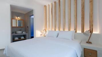 Una camera da letto con un letto grande, un pannello murale in legno, un comodino con una lampada e un bagno con un lavandino e uno specchio.