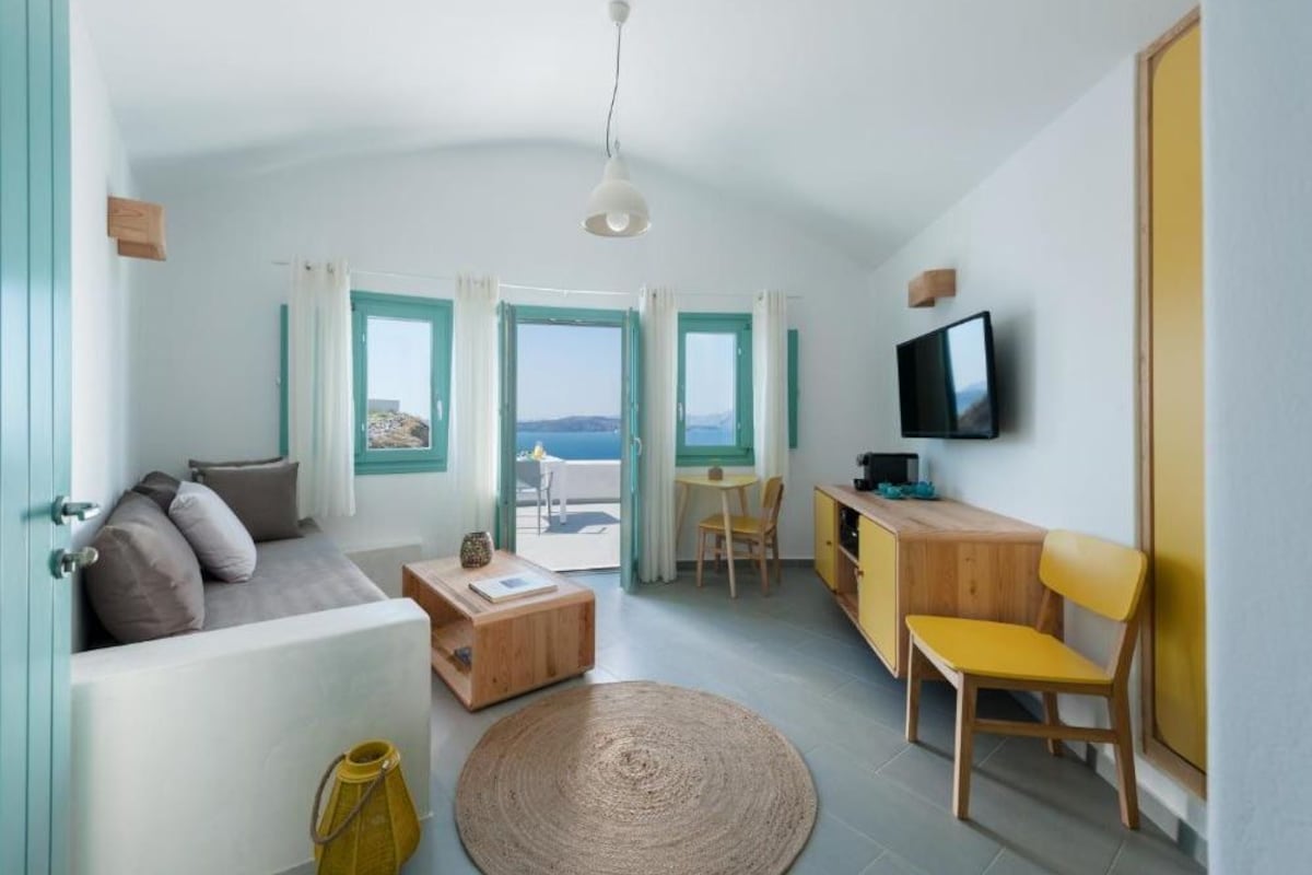 A compact living space with a sofa, a small dining table, a TV, and a view of the sea through large windows.
