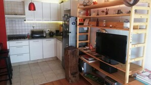 Una cocina compacta con armarios blancos, una lámpara colgante roja y una estantería de madera con diversos objetos.