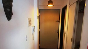 Un pasillo estrecho con suelo de madera, una puerta cerrada al final y un teléfono instalado en la pared.