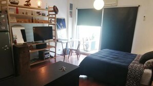 Una habitación pequeña con una cama, un escritorio con computadora, un televisor y una mesita.