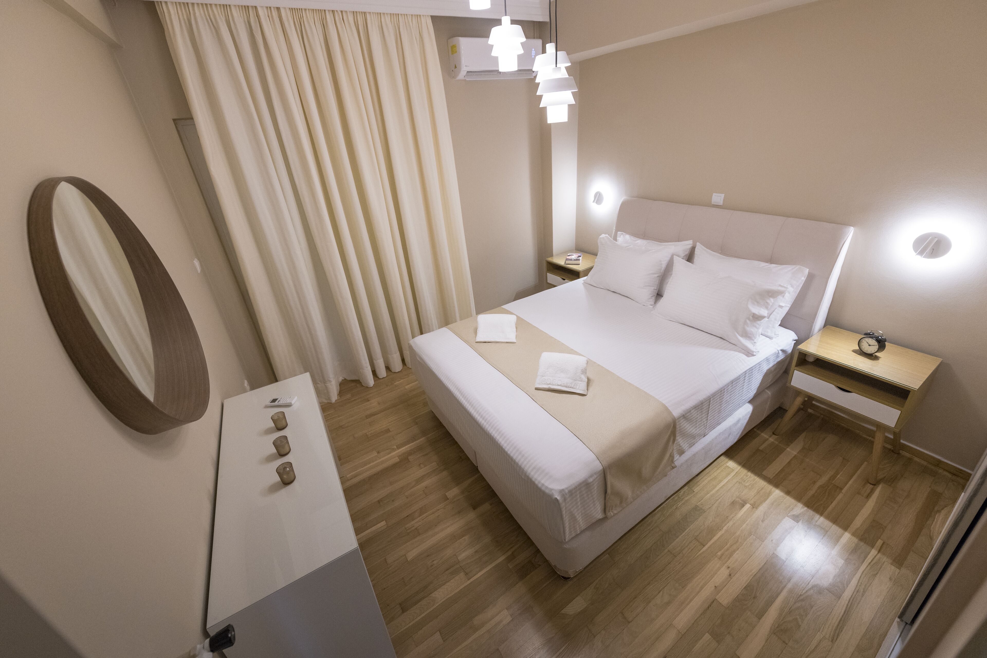 Una habitació d'hotel moderna amb un llit gran, taules de nit, un mirall i una làmpada al sostre.