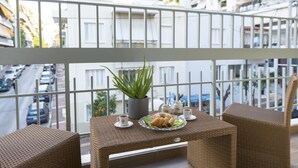 En balkon med fletmøbler, en potteplante og et bord dækket med kager og kopper.