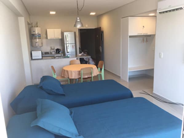 A compact room with two beds, a small kitchen area, and a dining table.