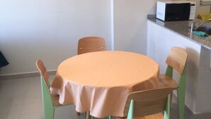 A dining area with a round table covered by a peach-colored tablecloth, surrounded by four chairs with green legs. A tall, narrow pendant light hangs above the table. - Bulnes & Cabrera (Buenos Aires)