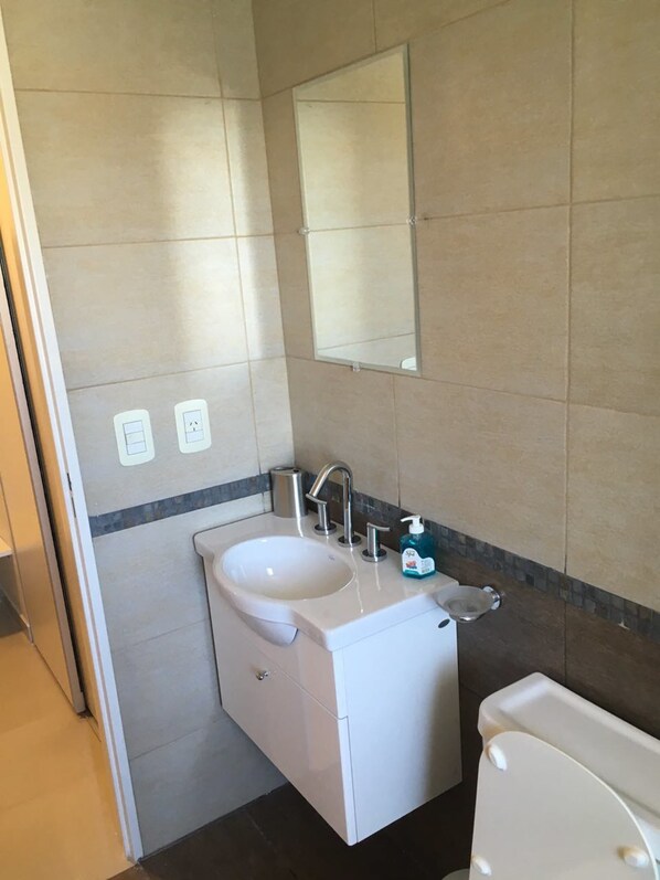 A bathroom with a white sink, mirror, and toilet. There are two electrical outlets on the wall.