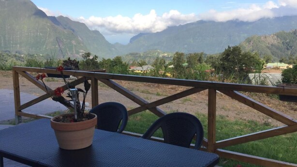 An outdoor patio with a table and chairs, a potted plant, and a view of mountains. - Ô Coeur De l'île (Salazie)