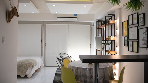 A modern room with a bed, a dining table, and chairs. There is a whiteboard, a plant, and framed pictures on the wall. - Cabrera & Gascon (Buenos Aires)