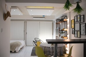 A modern room with a bed, a dining table, and chairs. There is a whiteboard, a plant, and framed pictures on the wall.