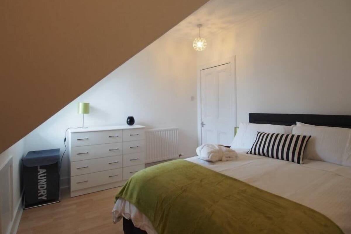 A bedroom with a bed, a dresser, a radiator, and a laundry bag.