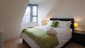 A bedroom with a bed, a window, and a nightstand with a lamp. - Thistle Apartments (Aberdeen)