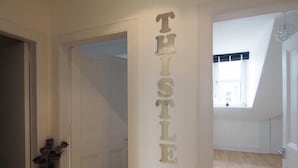 A hallway with a white door, a wall-mounted sign reading "THISTLE 4", and a window with a view of the outside. - Thistle Apartments (Aberdeen)