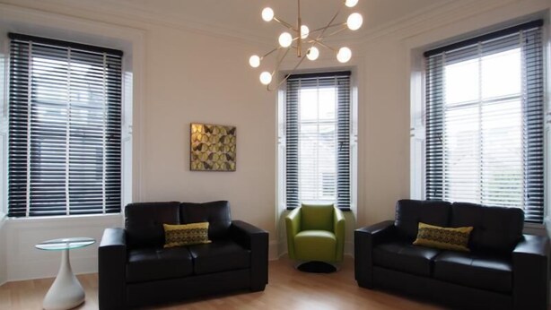 A spacious living room with two black sofas, a green armchair, and a small white table. - Thistle Apartments (Aberdeen)