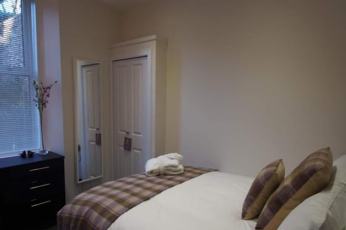 A bedroom with a bed, a dresser, a window with blinds, and a door.