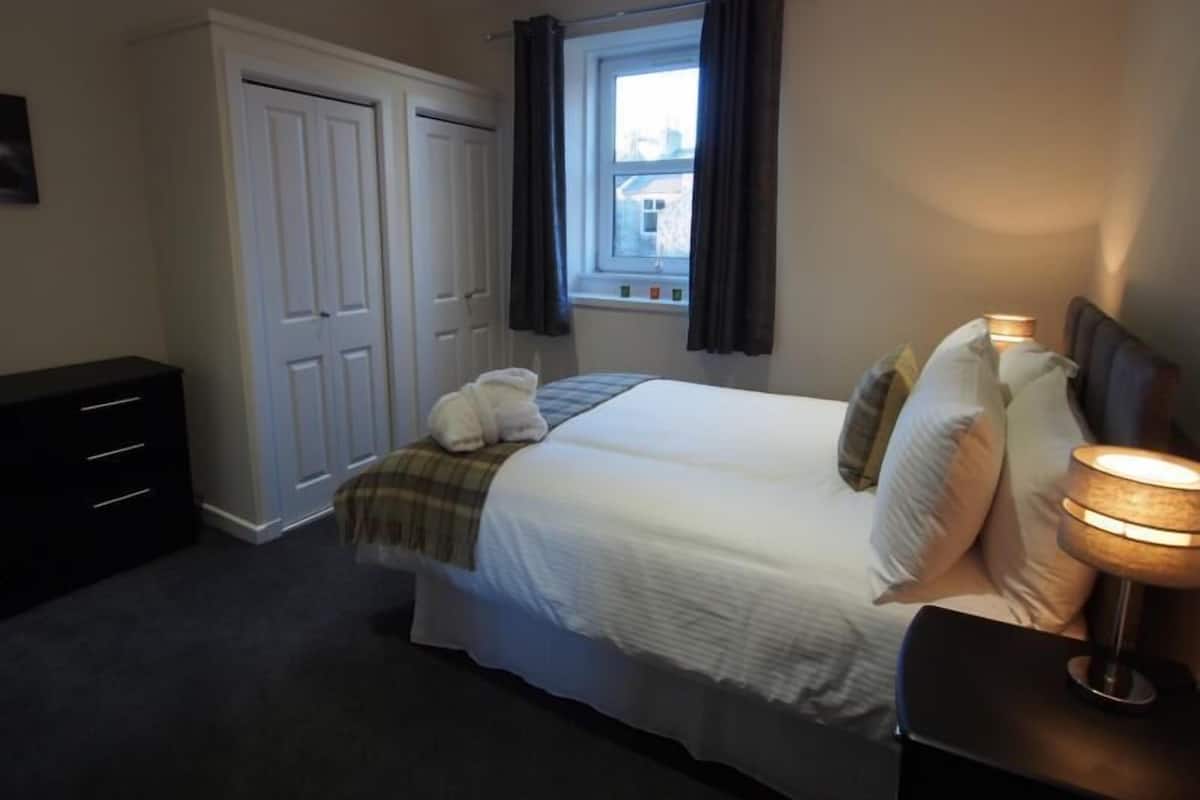 A bedroom with a bed, bedside lamp, and a window with curtains.