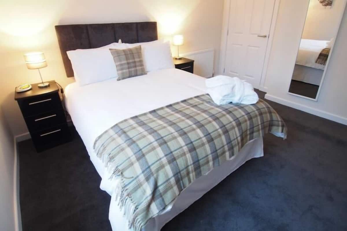 A neatly made bed with a plaid blanket, two bedside lamps, and a mirror on the wall.