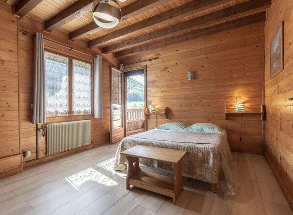 Ein Schlafzimmer einer Holzhütte mit Bett, Bank, Heizkörper und einem Fenster mit Vorhängen.