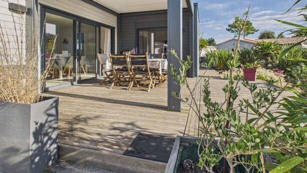 Una casa moderna con un patio cubierto, terraza de madera y plantas en macetas.