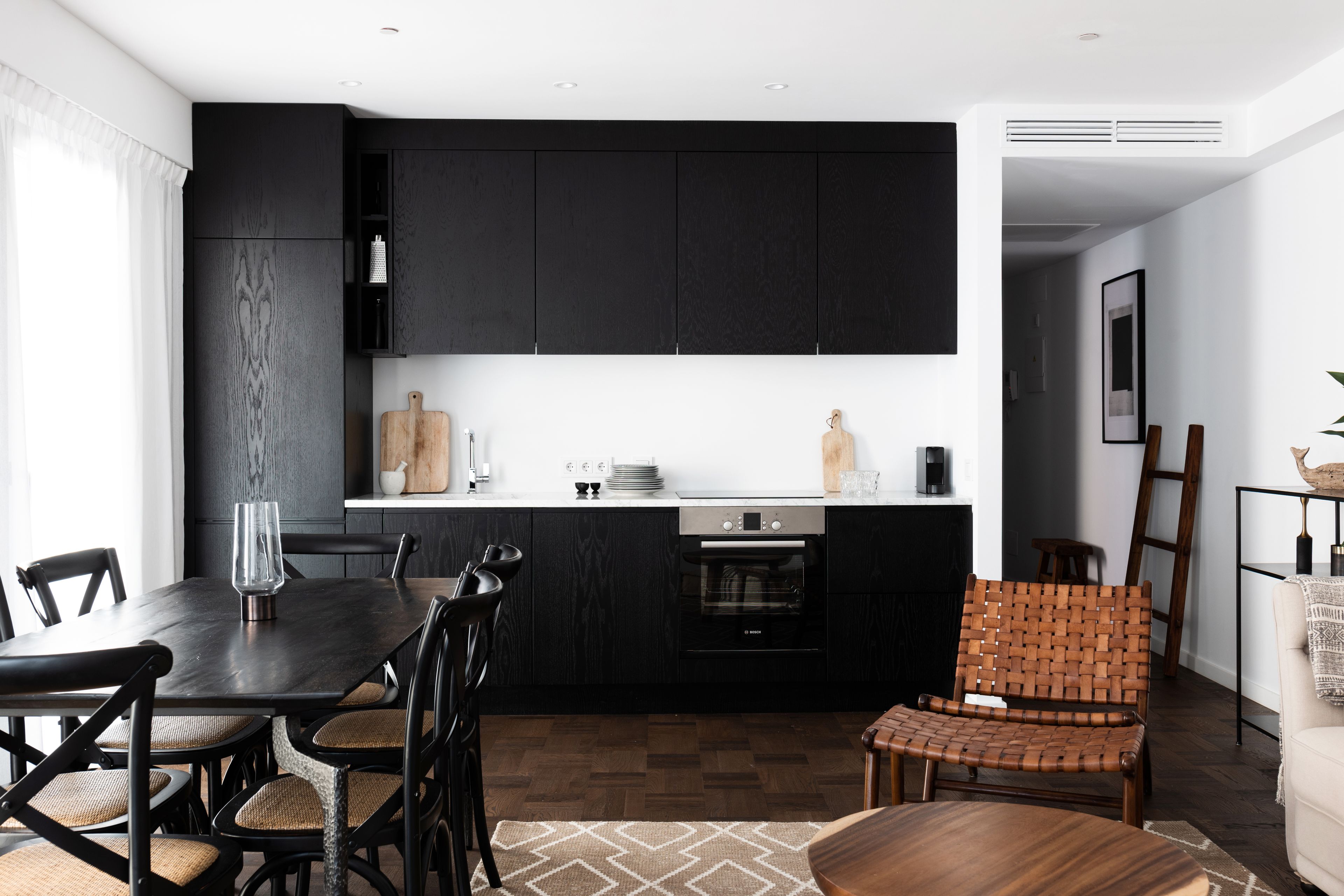 Una cocina moderna con armarios oscuros, una mesa de comedor con sillas y una silla de madera con respaldo trenzado.