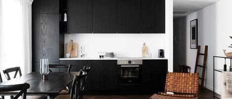 A modern kitchen with dark cabinetry, a dining table with chairs, and a wooden chair with a woven backrest.