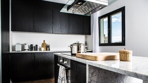 A modern kitchen with dark cabinetry, a marble countertop, and a window with a view. - Terreno Suites (Palma de Mallorca)