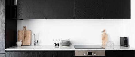 Una cocina moderna con armarios oscuros, encimera blanca y electrodomésticos de acero inoxidable.