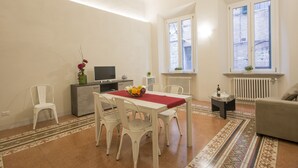 Un comedor con una mesa, sillas y un televisor. Hay ventanas con vistas al exterior.