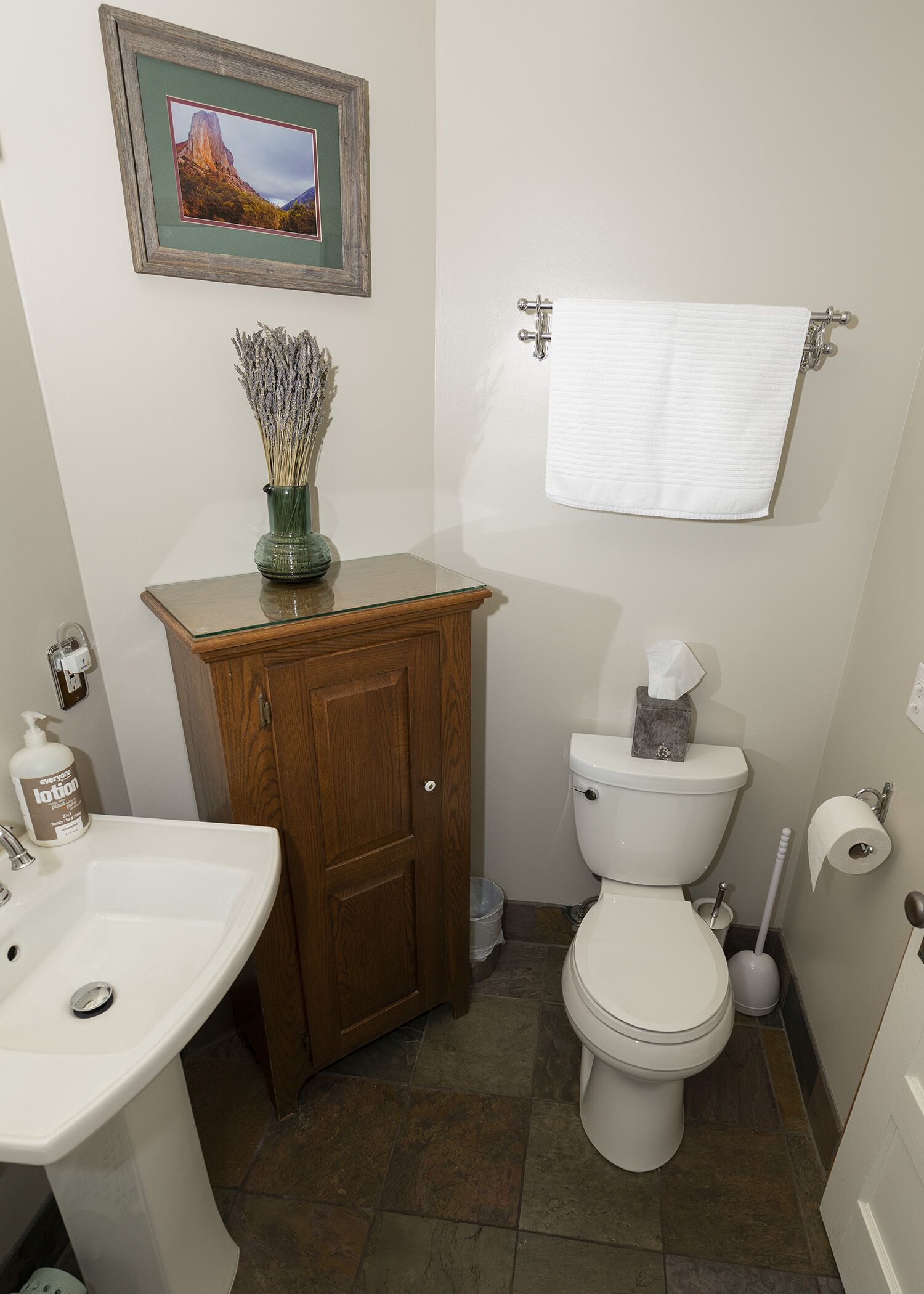 A bathroom with a wooden cabinet, a white sink, a toilet, and a framed picture on the wall.