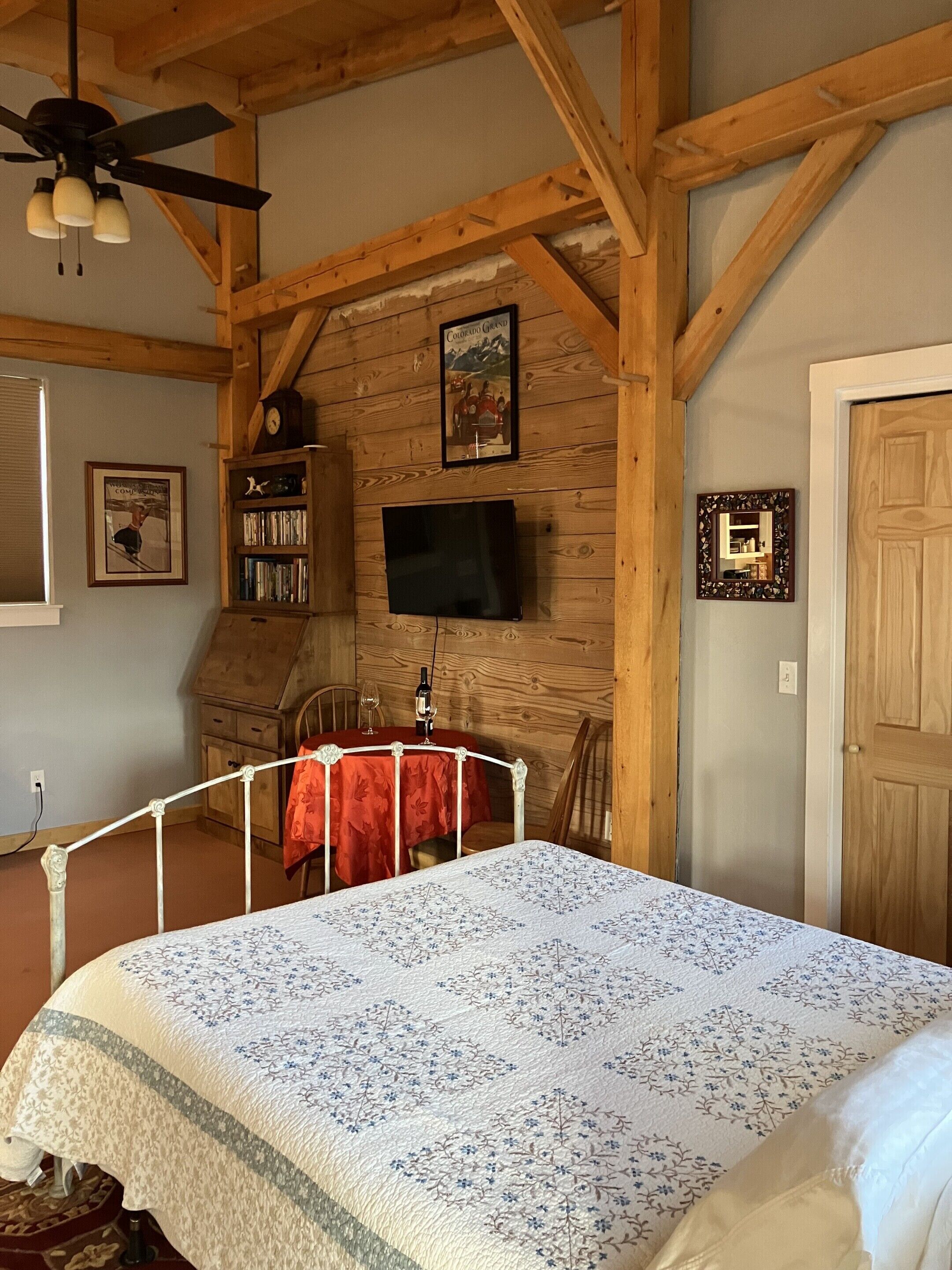 Een slaapkamer met een bed, houten balken, een televisie, een boekenkast en een deur.