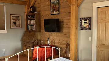 Een slaapkamer met een bed, houten balken, een televisie, een boekenkast en een deur.