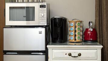 Una kitchenette con microondas, cafetera y un mueble pequeño.