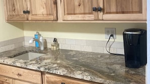 Une cuisine avec des meubles en bois, un plan de travail en granit, une machine à café et un distributeur d’eau.