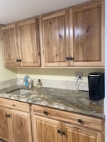 A kitchen with wooden cabinets, a granite countertop, a coffee maker, and a water dispenser.