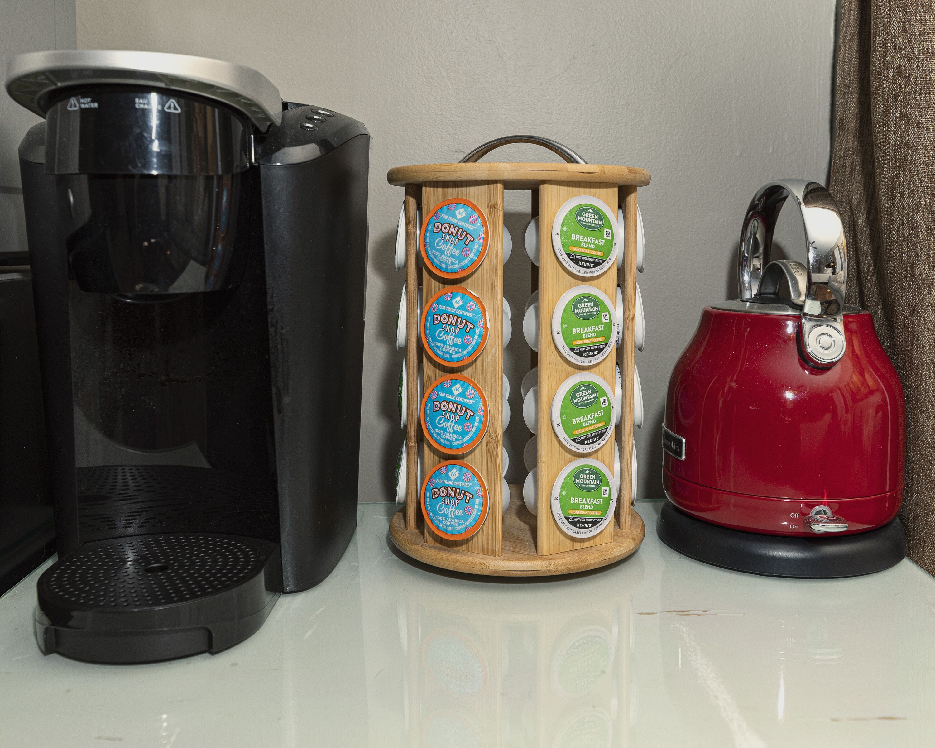 Una macchina per il caffè, un contenitore di legno con capsule di caffè e un bollitore rosso su un piano di lavoro.
