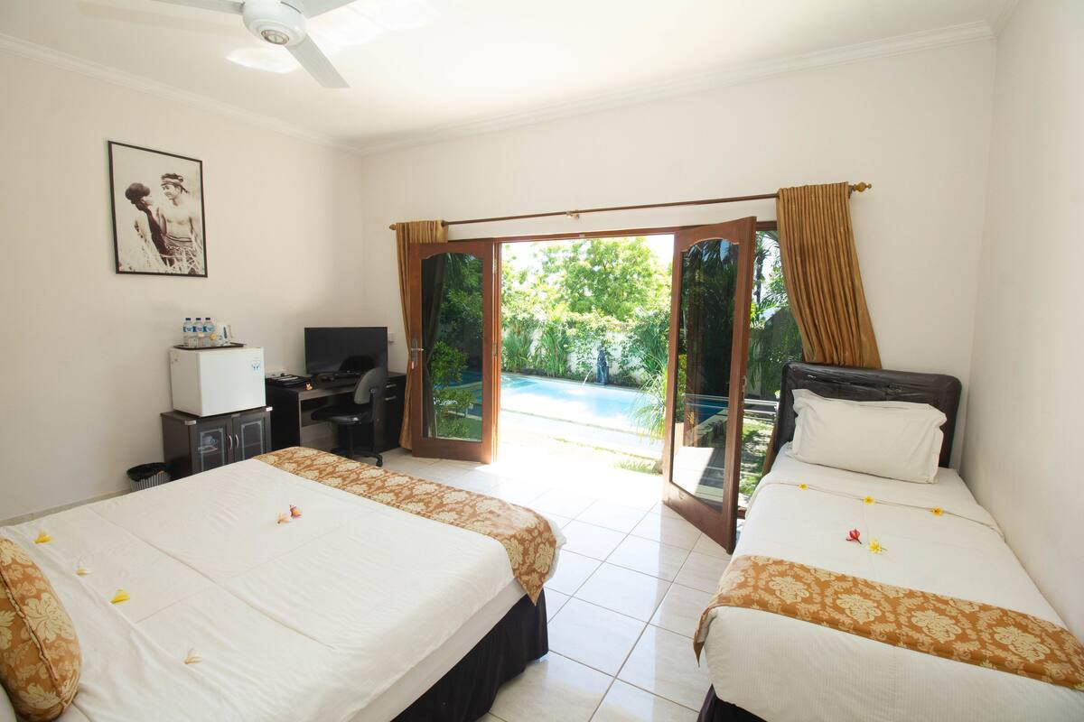 A hotel room with two beds, a desk, a television, and a view of a swimming pool.