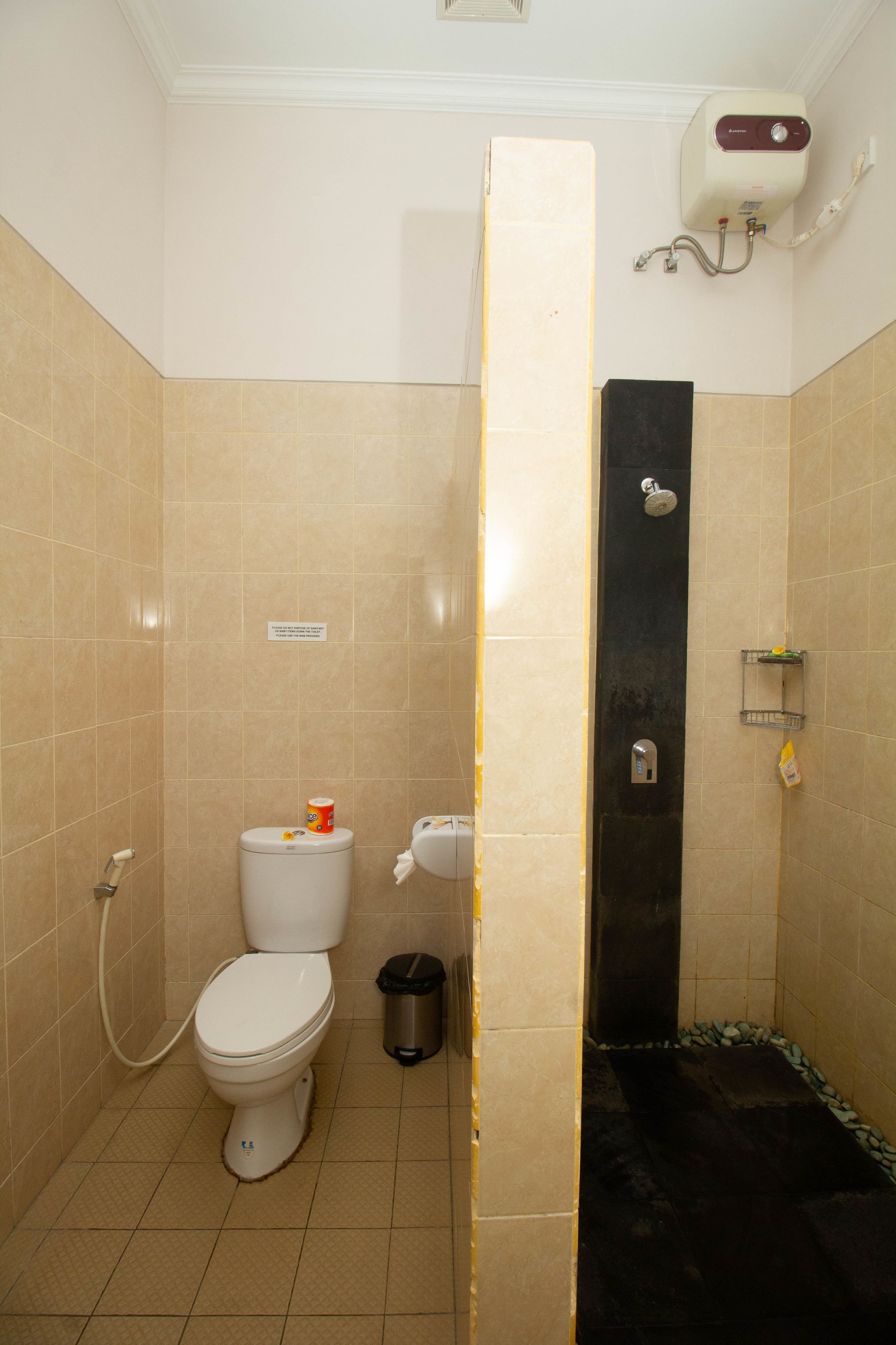 A bathroom with a toilet, a trash bin, a shower, and a towel dispenser.